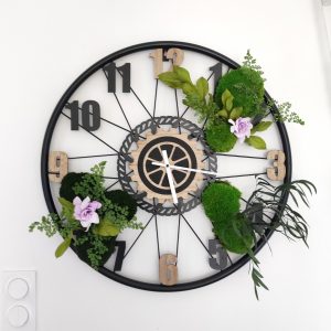Horloge murale végétale 64 cm structure métal noir et bois naturel, mousses stabilisées, fougères, feuillages tropicaux et gardénias mauves – mécanisme silencieux, pièce unique, livraison France